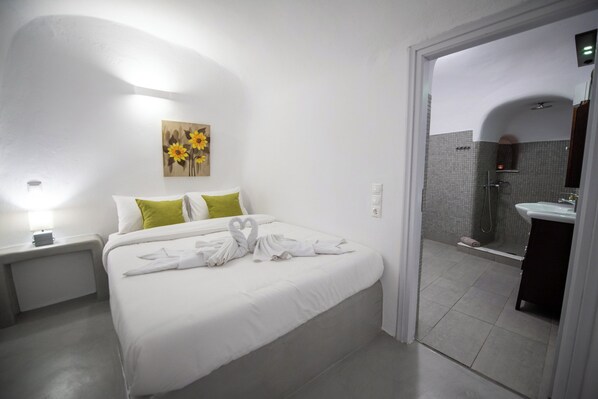 Habitació d'hotel amb un llit ben tendit, un quadre de girassols a la paret i un bany visible a través d'una porta oberta.
