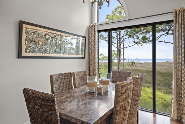 A dining area with a large table, wicker chairs, and a framed artwork on the wall. - Bay Views- Heron Walk Sandestin®, Golf Cart, Beach, Pool (Miramar Beach)