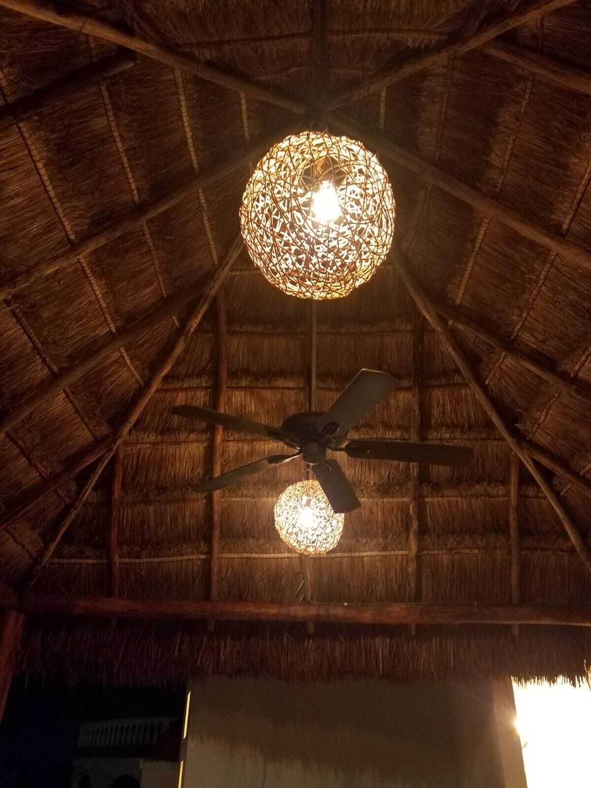 A room with a thatched ceiling, a ceiling fan, and a decorative light fixture.