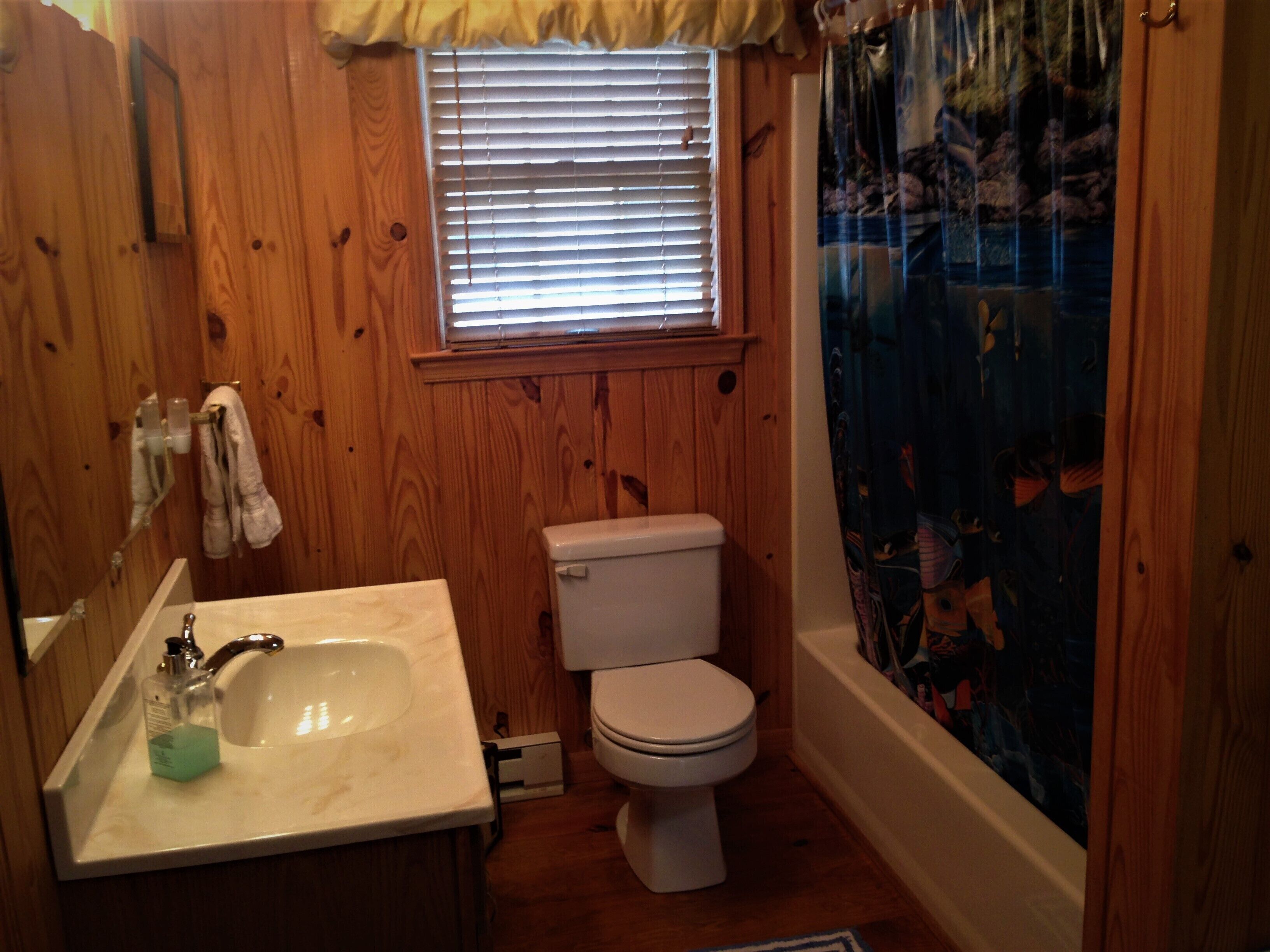 A bathroom with wooden walls, a toilet, a sink, and a window with blinds.