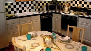 Une cuisine avec un dosseret à carreaux, des armoires blanches, un four à micro-ondes, une cuisinière et une table à manger mise avec des assiettes, des verres et un coquillage décoratif.