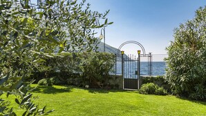 A coastal garden with a metal gate, a lamp post, and a view of the sea. - BEUST HOUSE - ADA - Balcony overlooking lake, harbor and village (Nago-Torbole)