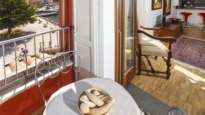 A balcony with a view of a marina and buildings, a wooden chair, a table with bread, and a kitchen area with red bar stools. - BEUST HOUSE - ADA - Balcony overlooking lake, harbor and village (Nago-Torbole)