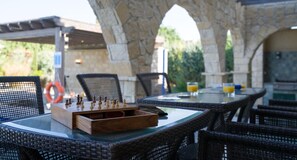 Un espace extérieur aménagé pour les repas, avec des meubles en osier et un jeu d’échecs.