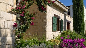 A stone building with a window and a door, surrounded by lush greenery and flowers. - Villa 141 Rio - Five Bedroom Villa, Sleeps 10 (Kouklia)