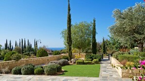 A landscaped garden with a stone pathway, various shrubs, and tall trees. - Villa 141 Rio - Five Bedroom Villa, Sleeps 10 (Kouklia)