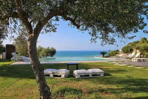 A poolside area with lounge chairs and a small table, overlooking a clear blue sea. - Modern property with Private Golf Practice, Private Pool, Garden, WiFi, Sea VIew (Campofelice Di Roccella)