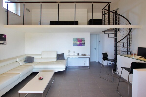 A modern loft apartment with a white sofa, a small dining table, and a staircase leading to an upper level. - Modern property with Private Golf Practice, Private Pool, Garden, WiFi, Sea VIew (Campofelice Di Roccella)