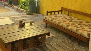Una habitación pintada de amarillo con un banco de madera, una mesita con una tetera y plantas en macetas.