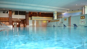 Una piscina interior con agua cristalina, una escalera que sube a un segundo nivel y murales decorativos en las paredes.