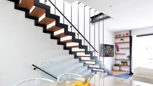 A modern interior with a staircase, a dining area with a glass table, and a living space with a sofa and shelves. - CASA DEL MAR 50m from the beach (Tamariu)