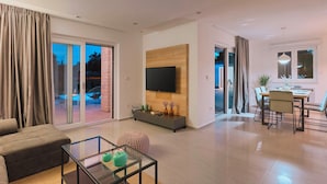A modern living room with a sofa, a glass coffee table, a flat-screen TV mounted on a wooden panel, and a dining area with a table and chairs. - Villa Monte in Breg (Haus für 6 Personen) (Labin)
