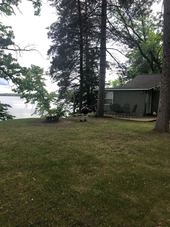 A grassy area with a small deck and a grill, overlooking a body of water.