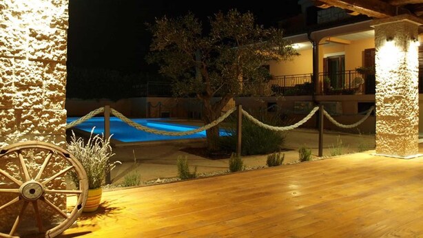 Um deck de madeira com barreira de corda, piscina e um edifício ao fundo.