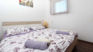 Quarto com cama, mesa de cabeceira, abajur, janela com cortinas e um quadro na parede.