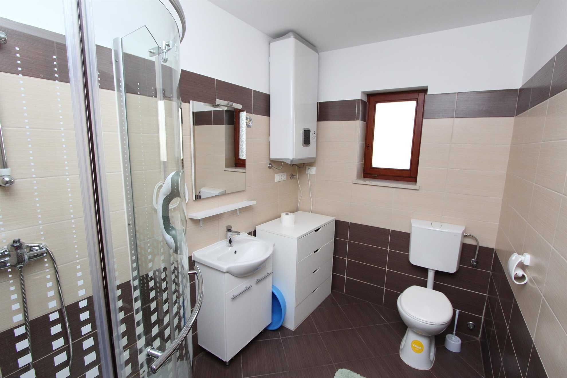 A bathroom with a glass shower enclosure, a white sink, a toilet, and a window.