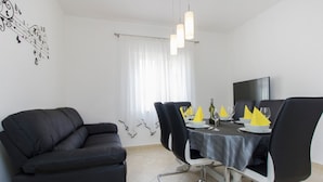 A dining area with a black sofa, a dining table set with plates, glasses, and a bottle, and a TV on the wall. - Apartment in Grebaštica with Seaview, Terrace, Air condition, WIFI (886-3) (Grebaštica)