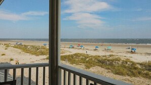 A beach view from a covered area with a railing, sandy beach, and umbrellas. - Port O'Call B 203, Direct Ocean View! (Isle Of Palms)