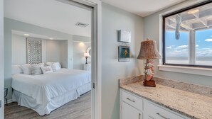 A bedroom with a bed, a nightstand, a lamp, and a window with a view of the sea. - Port O'Call B 203, Direct Ocean View! (Isle Of Palms)