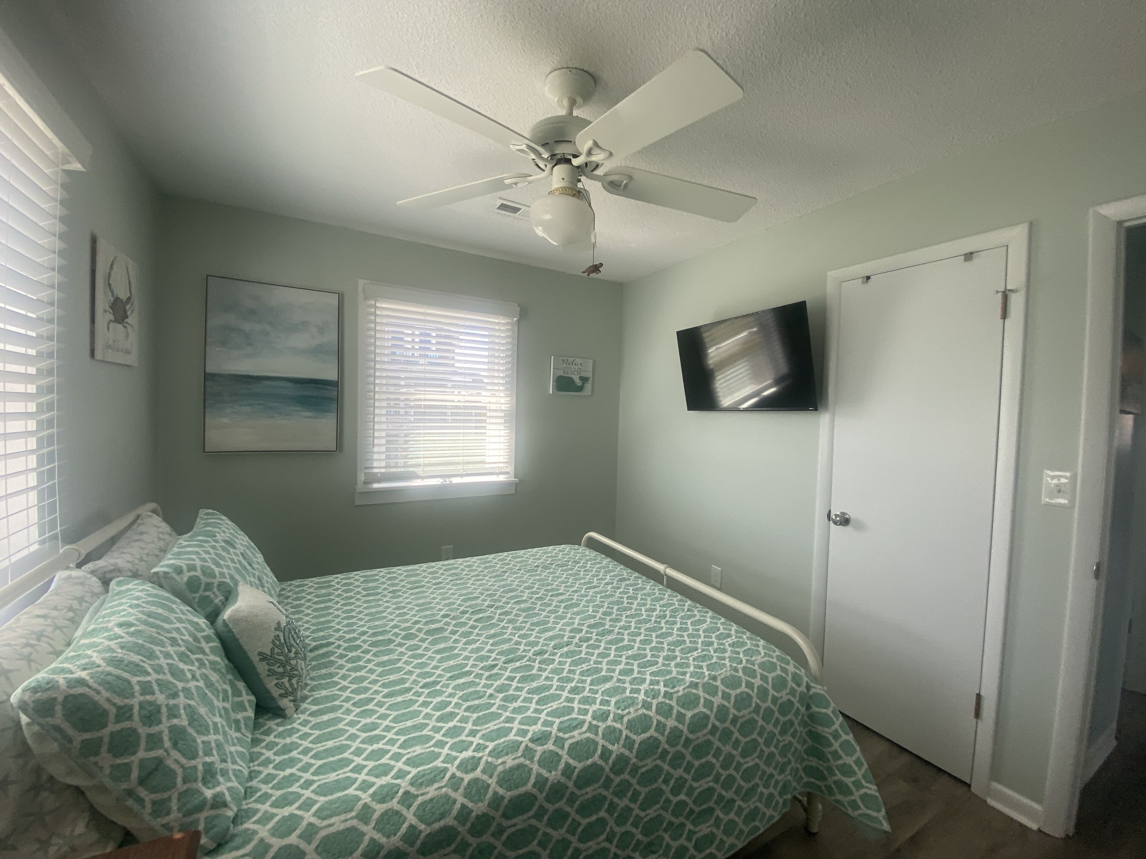 A bedroom with a bed, a ceiling fan, a TV, and a window with blinds.