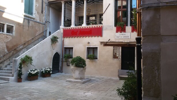 A courtyard with a staircase leading to a building with a red awning and a sign reading "Corte de'Ca' Amadi". - Sunny, quiet flat in the heart of Venice, near Rialto Bridge (Venezia)