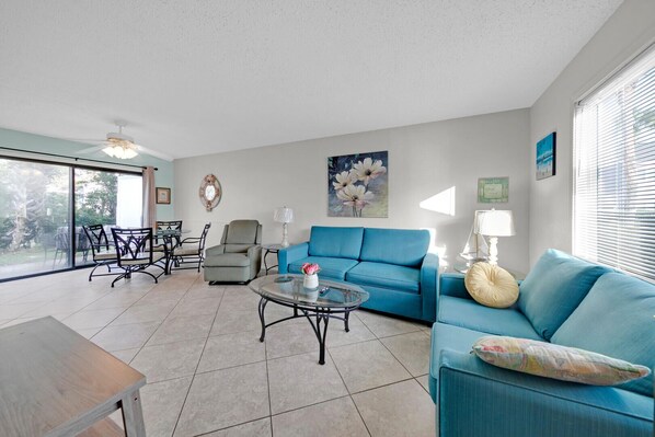 A spacious living room with a blue sofa, a round coffee table, and a dining area with chairs and a table.