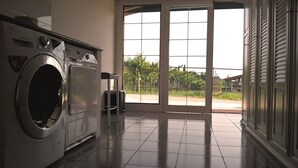 Uma lavanderia com máquina de lavar, lixeira e uma grande porta de vidro que dá para uma área externa.