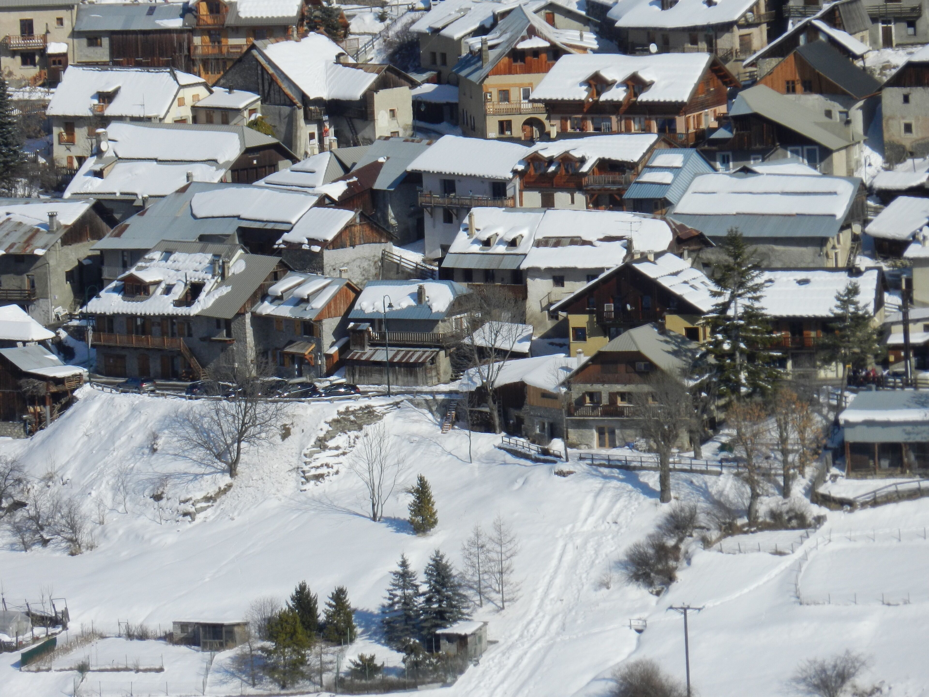 A snow-covered village with traditional wooden houses, a ski lift, and a clear view of the surrounding snowy landscape.