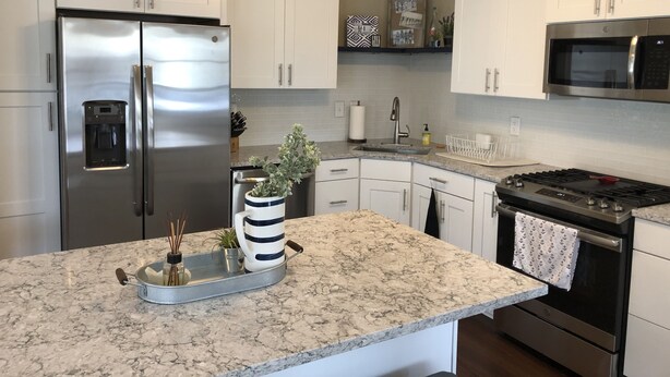 Una cocina moderna con armarios blancos, electrodomésticos de acero inoxidable, una encimera de mármol y un ventilador de techo.