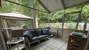 Ein überdachter Patio-Bereich mit einem blauen, gemusterten Sofa, einem kleinen Tisch und einem Schrank.