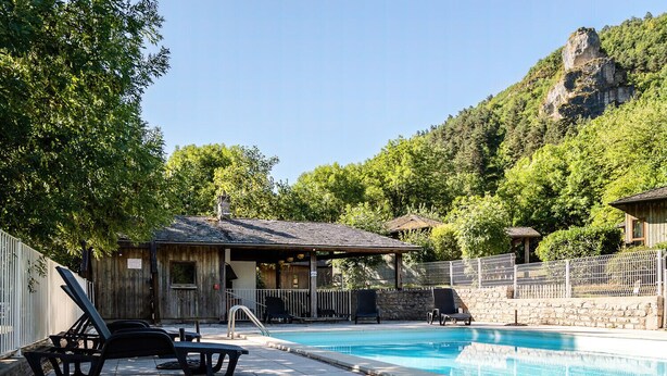 Un área de piscina con sillas de descanso, un edificio pequeño y un muro de piedra.