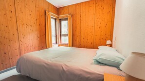 Un dormitorio con una cama grande, paredes de madera, una ventana con cortinas y una lámpara de noche.
