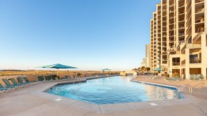 A pool area with lounge chairs and umbrellas, surrounded by a high-rise building. - Awesome Views and 10 Foot Ceilings in this Penthouse Unit on the 15th floor! (Orange Beach)