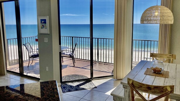 A room with a view of the beach, a dining area with a table and chairs, and a large window with a view of the ocean. - Awesome Views and 10 Foot Ceilings in this Penthouse Unit on the 15th floor! (Orange Beach)