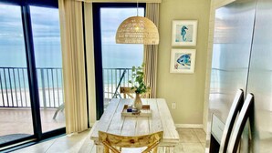 A dining area with a wooden table and chairs, a hanging light fixture, and a view of the ocean through large windows. - Awesome Views and 10 Foot Ceilings in this Penthouse Unit on the 15th floor! (Orange Beach)