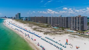A coastal hotel with multiple high-rise buildings, a beach with rows of umbrellas, and a clear view of the ocean. - Awesome Views and 10 Foot Ceilings in this Penthouse Unit on the 15th floor! (Orange Beach)