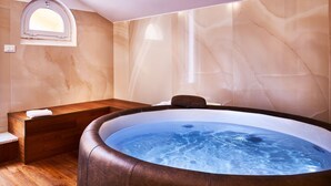 Une salle de spa dotée d’un bain à remous, d’un banc en bois et de murs en marbre.