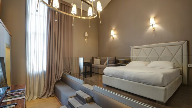 Une chambre moderne avec un grand lit, un lustre et un miroir qui reflète la pièce.