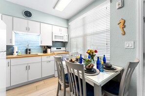 A modern kitchen with white cabinets, a microwave, and a dining area with a table set for two.