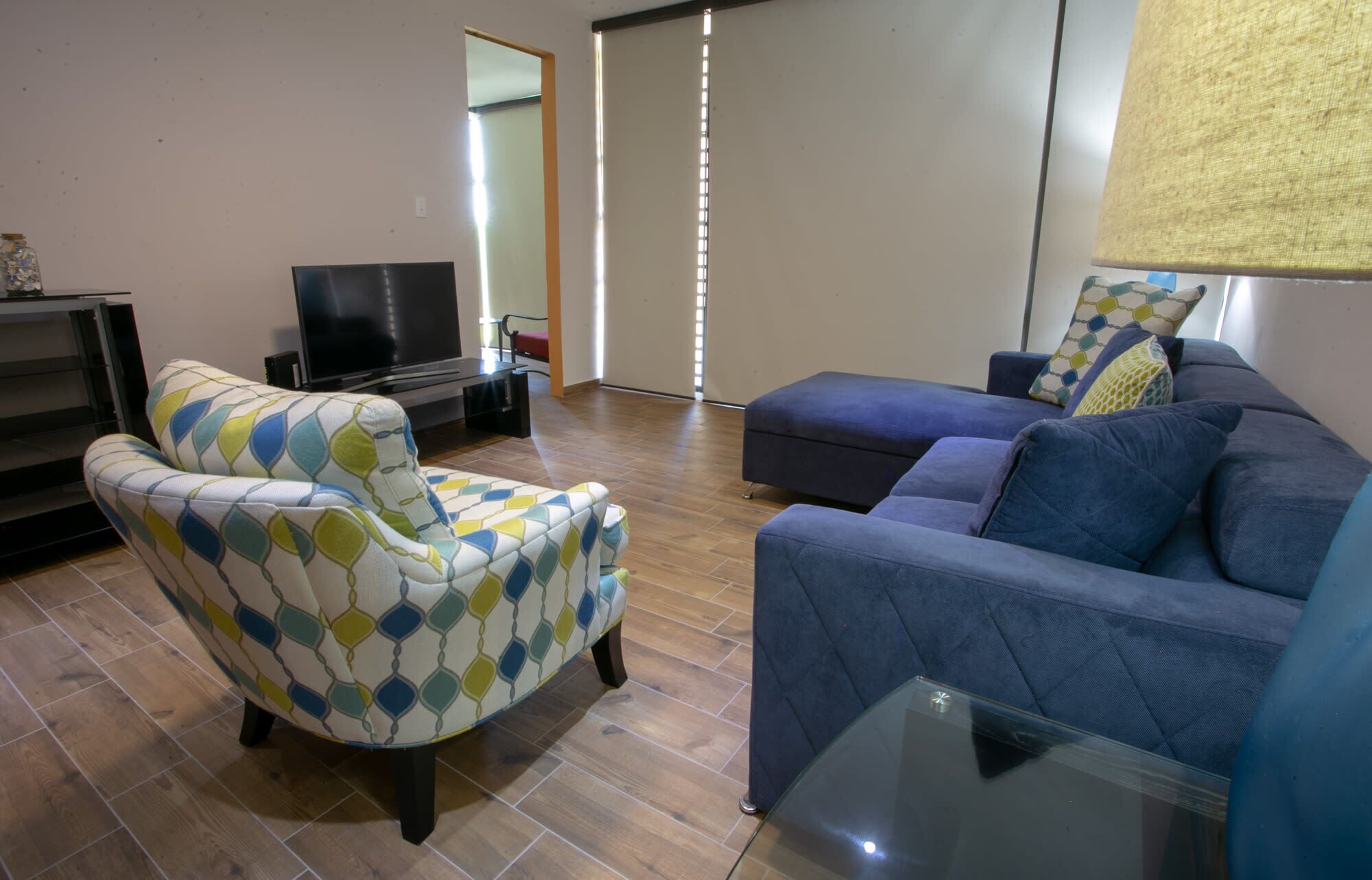 Una sala de estar con sofá, sillón, televisor y una mesa de centro de vidrio.