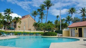 Una piscina con sillas de descanso, palmeras y un edificio con techo de tejas rojas.