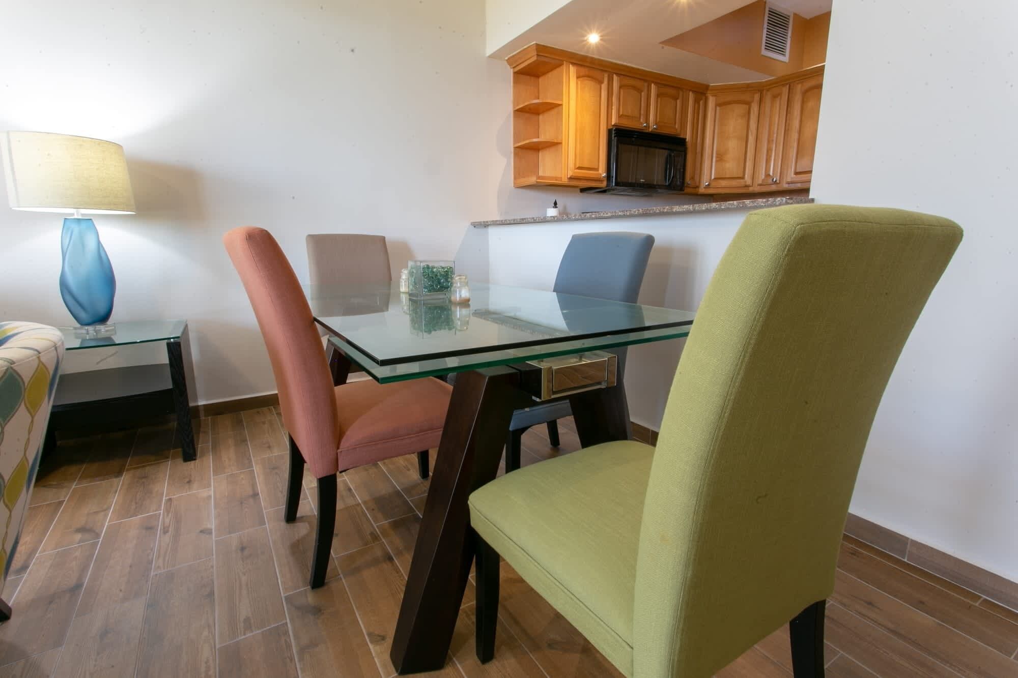 A dining area with a glass table and chairs, a lamp, and wooden cabinets above.