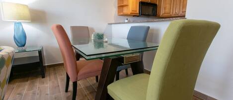 A dining area with a glass table and chairs, a lamp, and wooden cabinets above.
