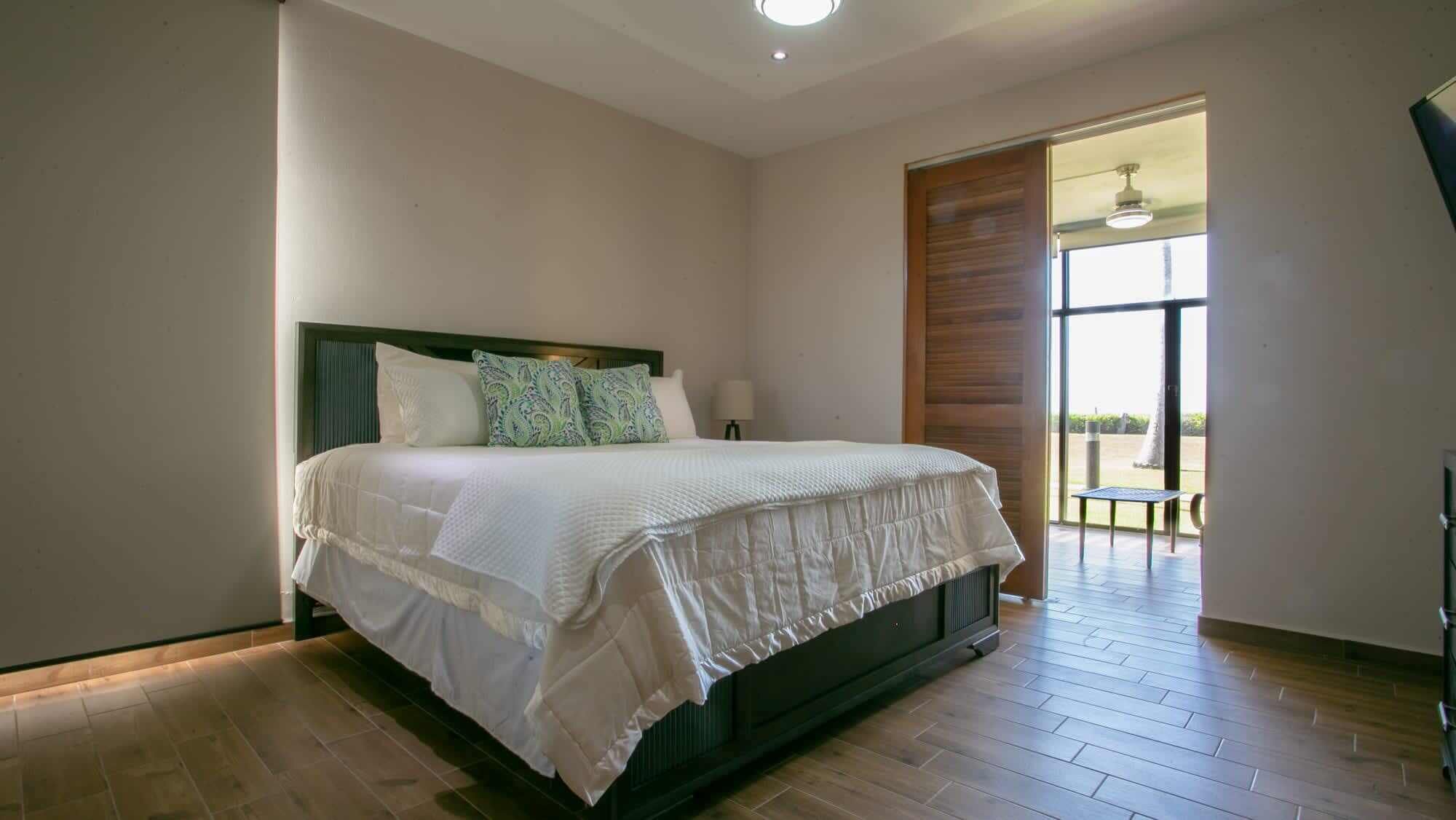 A bedroom with a large bed, a wooden headboard, a window with a view, and a door leading to an outdoor area.