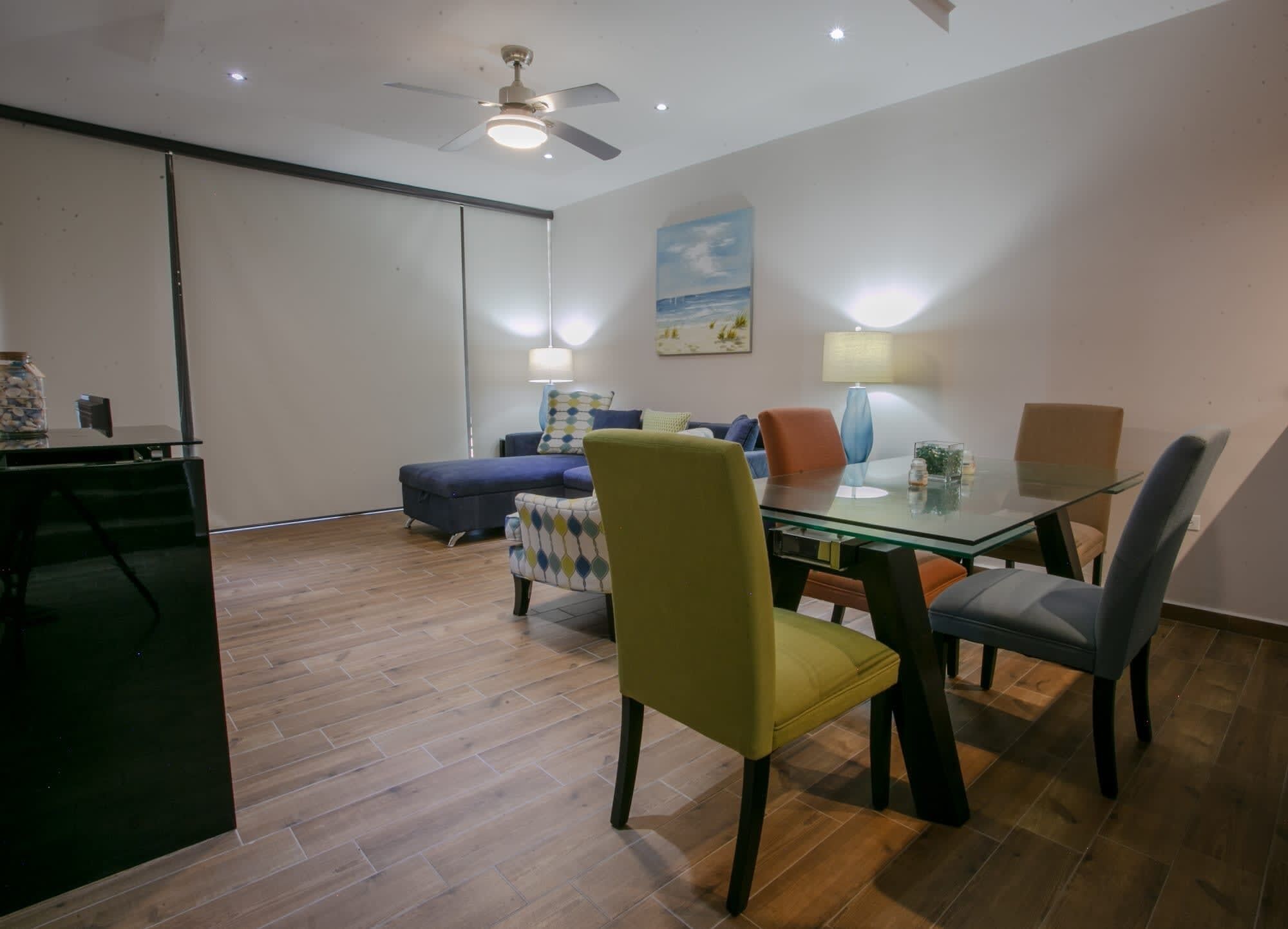 A dining area with a glass table, chairs, and a ceiling fan.