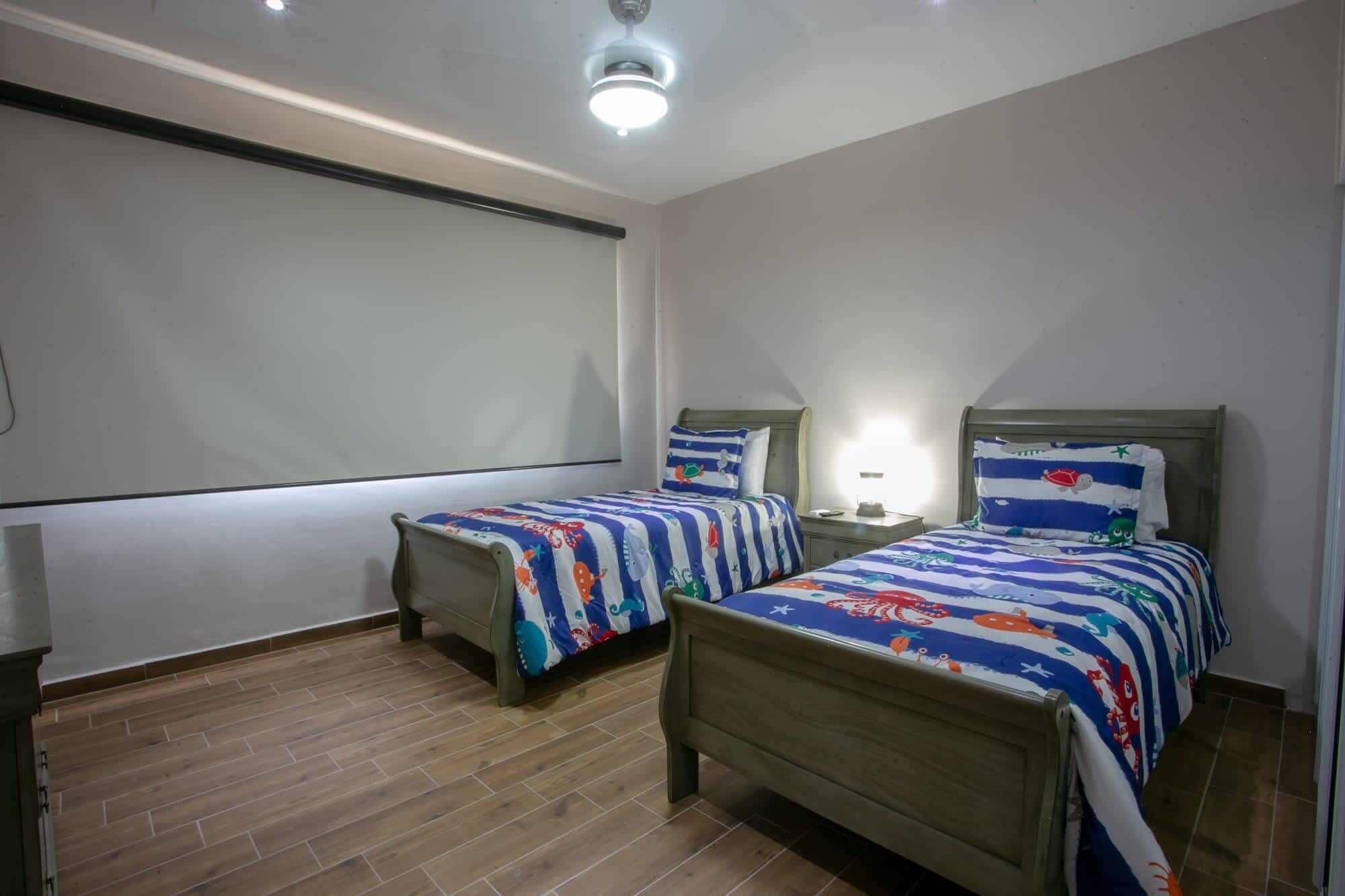 A bedroom with two single beds, wooden headboards, a nightstand with a lamp, and a ceiling light.