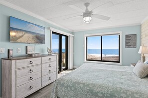 Une chambre dotée d’une grande fenêtre donnant sur la plage, d’un ventilateur de plafond et d’une commode avec des tiroirs.