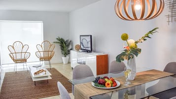 Ett modernt matområde med ett glasbord, två fåtöljer i rotting, en krukväxt och en dekorativ lampa.