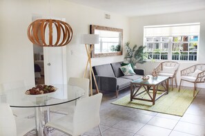 Un salon moderne avec une table à manger en verre, des chaises blanches, un canapé gris et une table basse en bois.