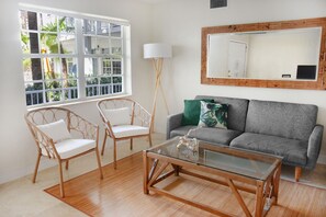 A living room with a glass coffee table, two white wicker chairs, a grey sofa with a green pillow, a floor lamp, and a large mirror on the wall. - 2 Bedroom Suite at Key Biscayne(4) (Key Biscayne)